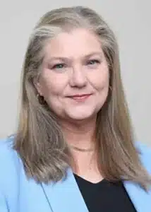 Smiling woman with long hair in blue blazer on neutral background.