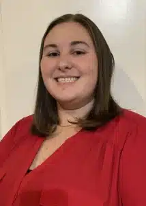 Smiling person with brown hair wearing a red blouse against a plain background.