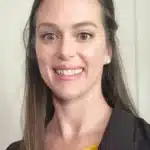 Smiling woman with long brown hair wearing a yellow top and dark blazer