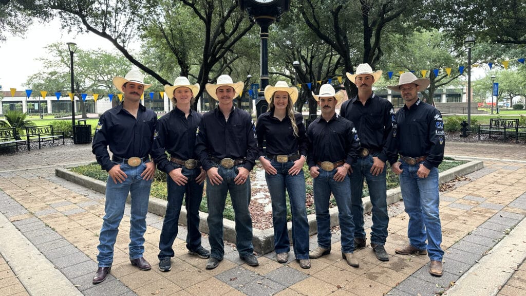 Seven McNeese student stand in the Quad wearing black rodeo shirts, boots, jeans and hats.