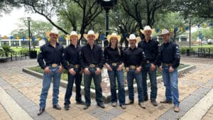Seven McNeese student stand in the Quad wearing black rodeo shirts, boots, jeans and hats.