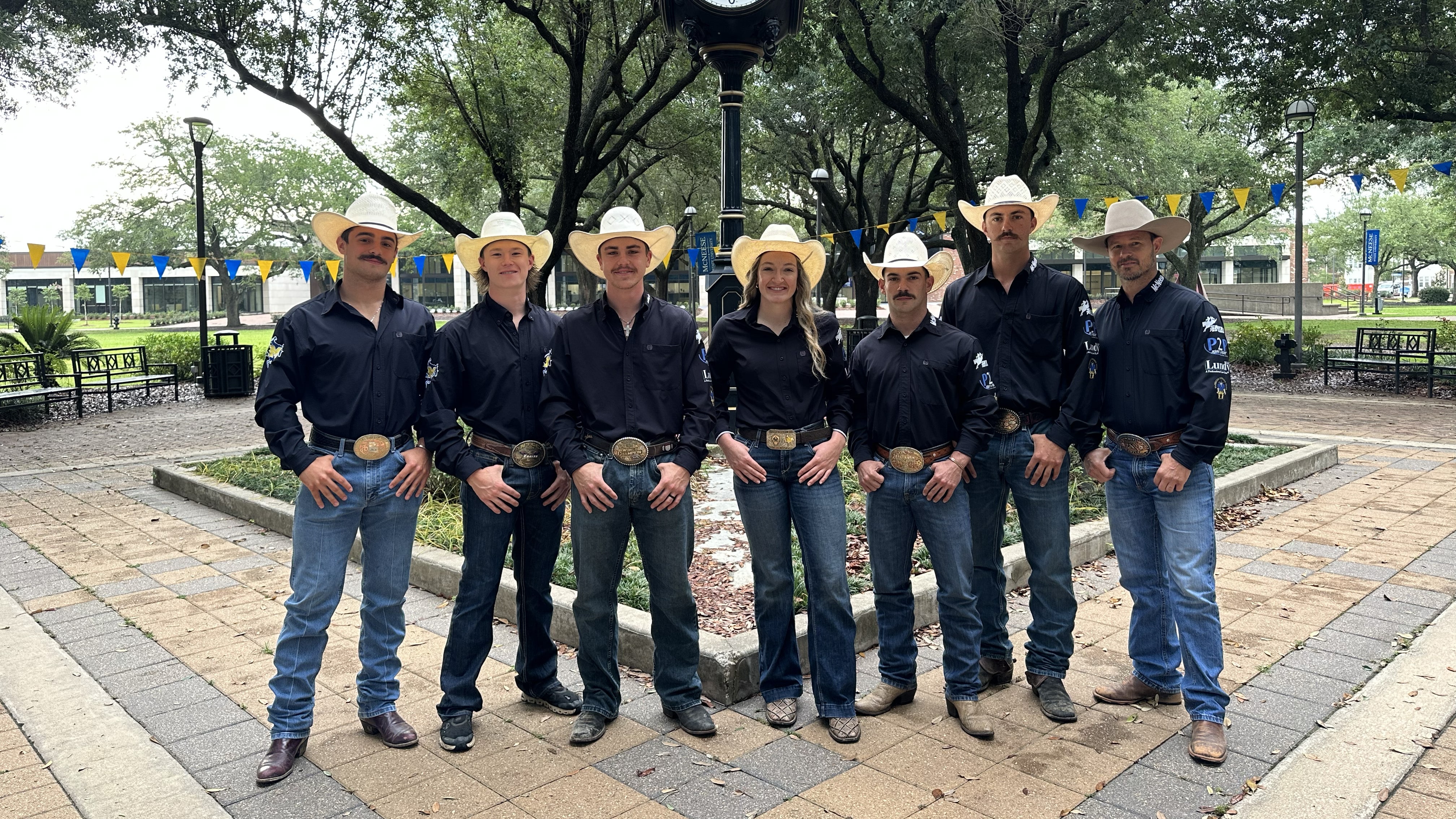 Seven McNeese student stand in the Quad wearing black rodeo shirts, boots, jeans and hats.