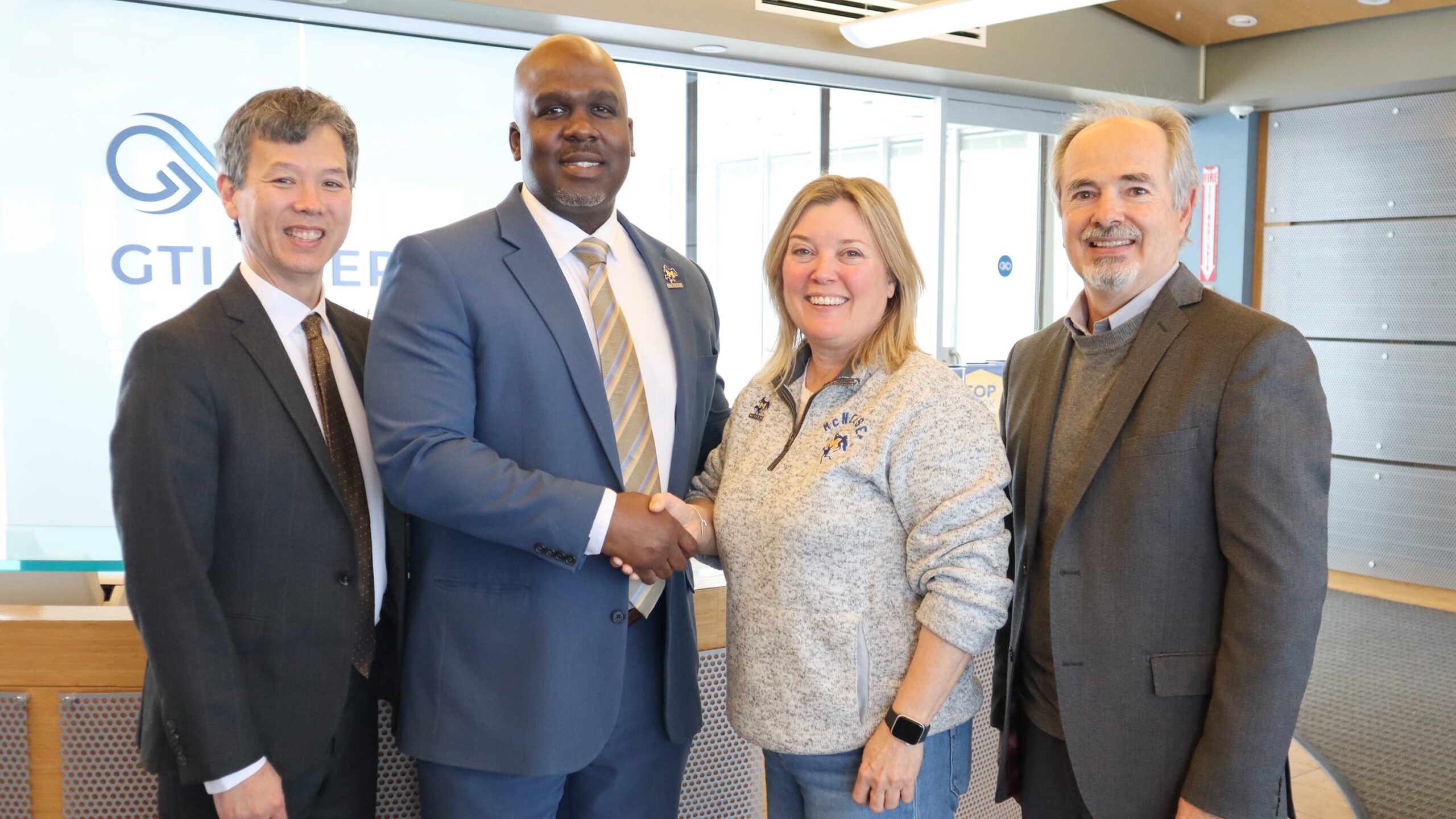 Four professionals smiling and shaking hands in an office setting.