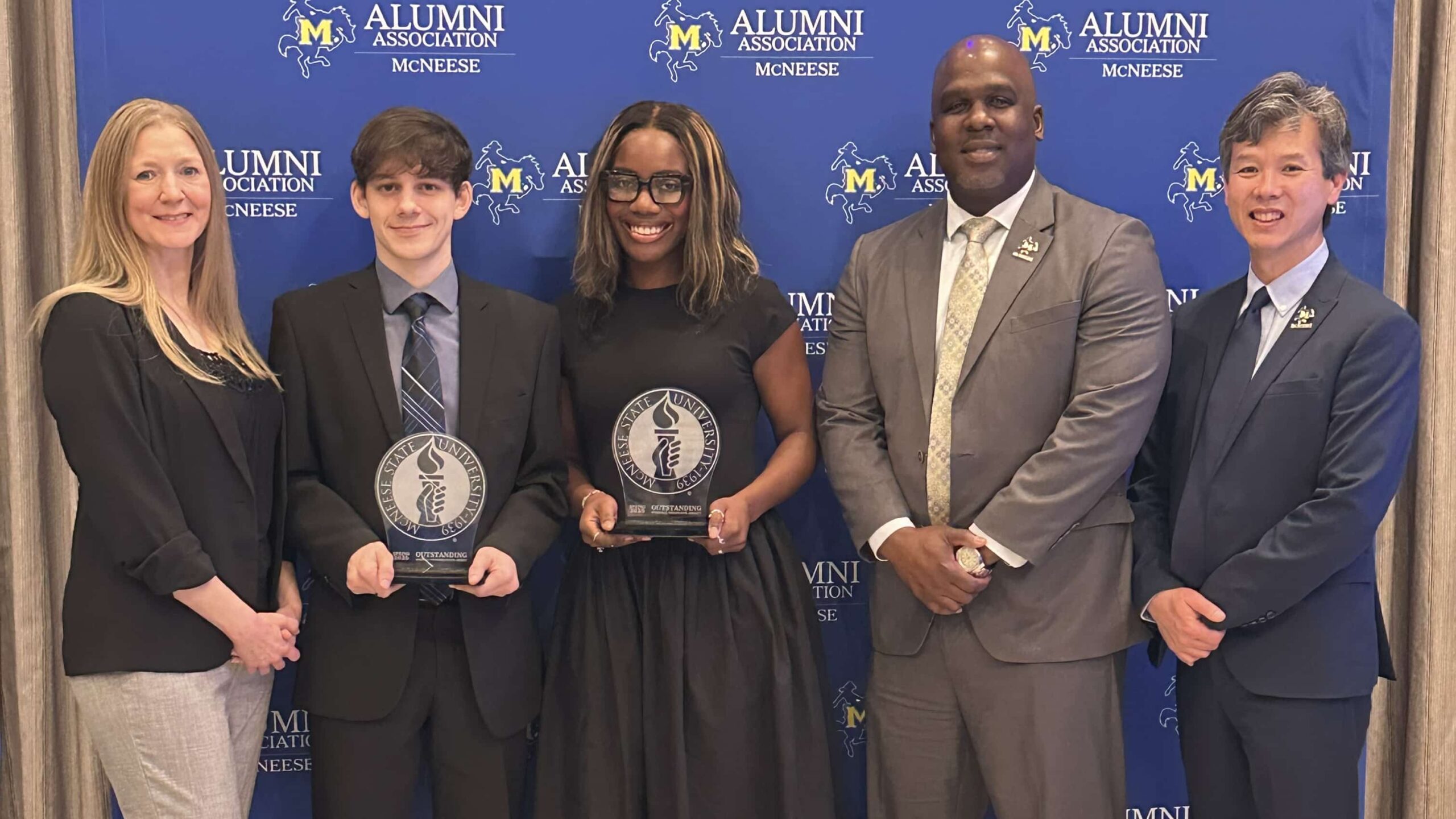 Group photo of McNeese State University Alumni Association award ceremony with two honorees holding plaques.