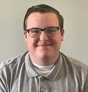 Smiling man wearing glasses and a gray polo shirt against a neutral background