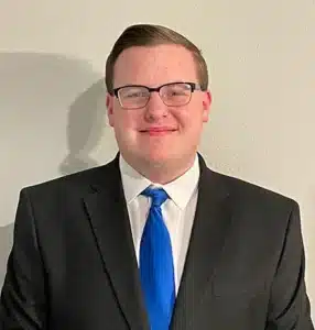 Man in suit and blue tie smiling against a white background.