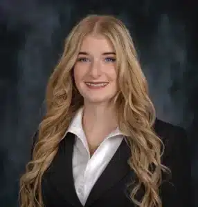 Woman with long blonde hair in professional attire smiling against dark background