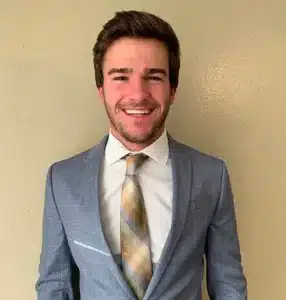 Smiling man in blue suit with patterned tie against beige background