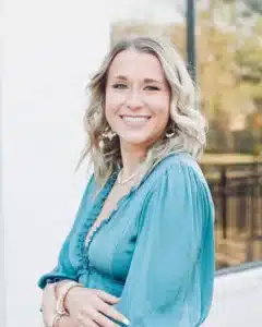Smiling woman with wavy blonde hair in a teal dress posing outdoors