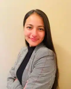Smiling woman with long hair in plaid blazer against a beige background.
