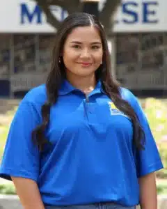 Person in blue polo shirt smiling outdoors with building in background.