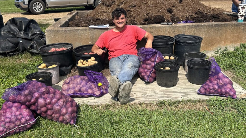 McNeese student Kayden Smith sitting on the ground surrounded by bags and buckets of potatoes.
