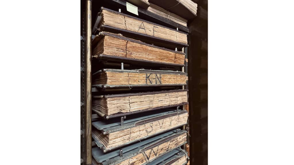 Old books that hold property records laying horizontally on a shelf.