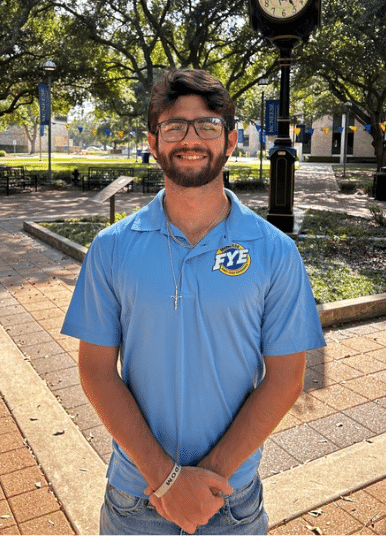 Aiden Winstead smiling outdoors in front of Clock Tower, wearing a light blue polo.