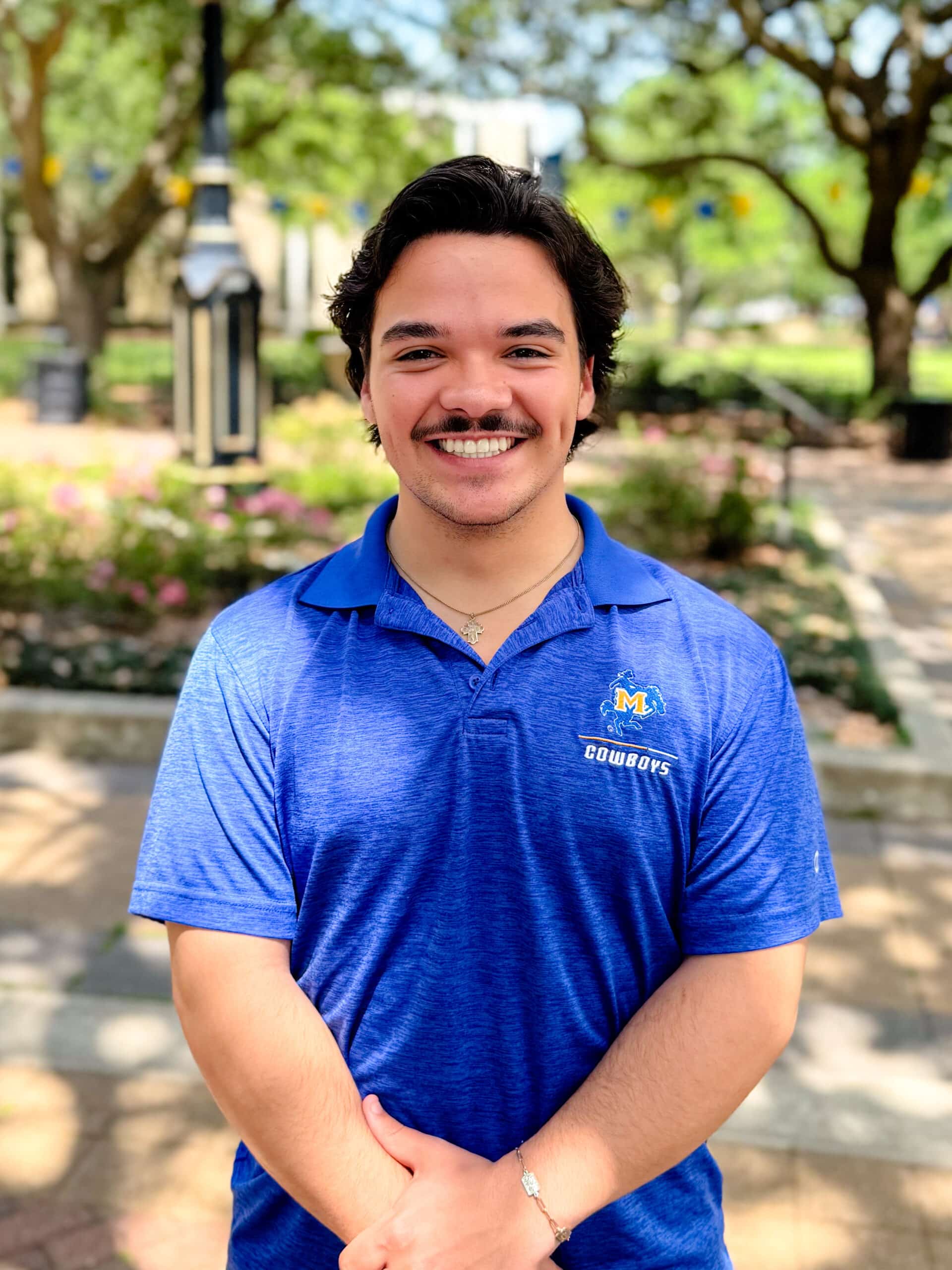 Andrew Dalton smiling outdoors in front of Clock Tower, wearing a blue polo.