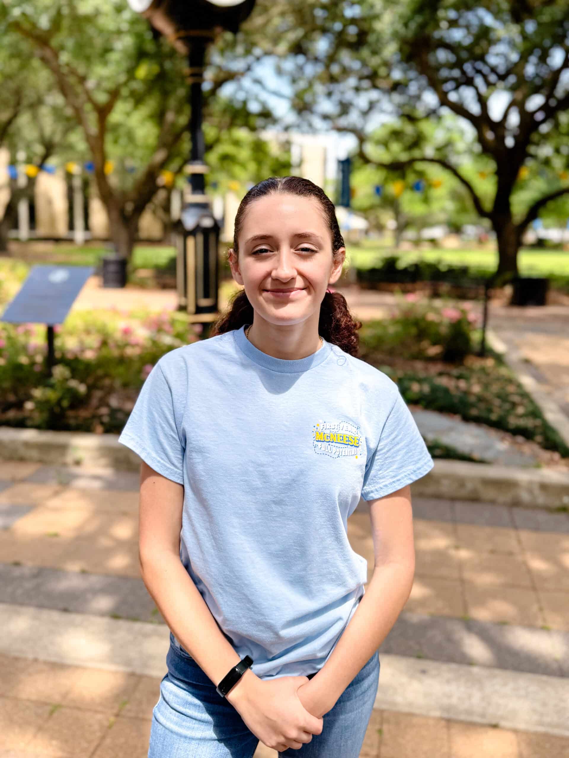 Victoria Clophus smiling outdoors in front of Clock Tower, wearing a light blue T-shirt.