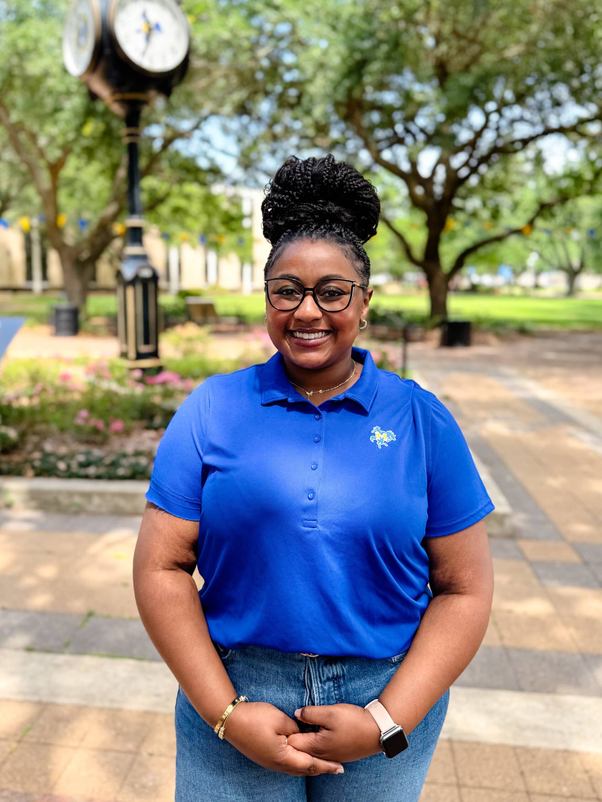 Samauria (Sue) Paddio smiling outdoors in front of Clock Tower, wearing a blue polo.