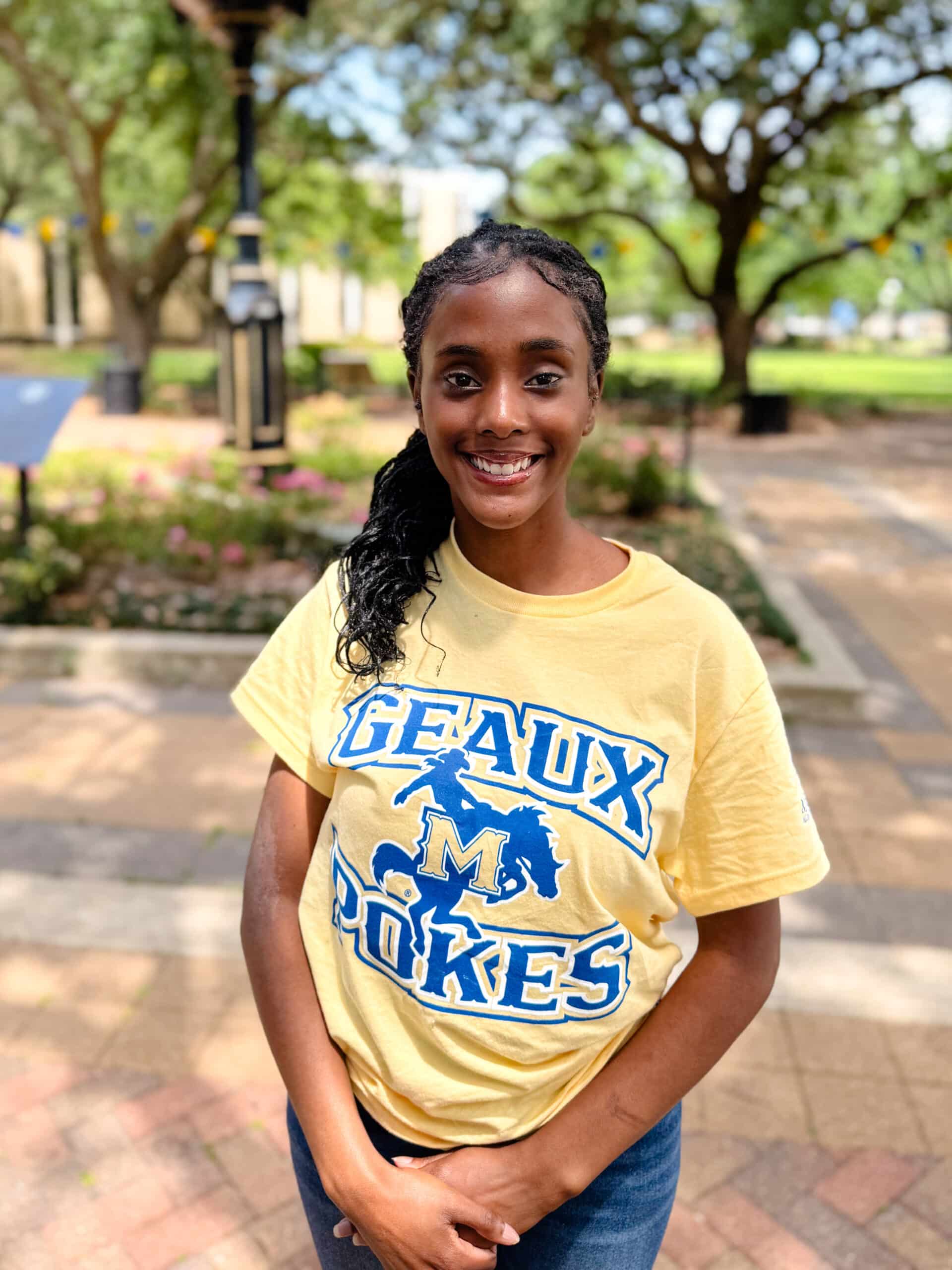 Seimone Freeman smiling outdoors in front of Clock Tower, wearing a bright yellow and blue T-shirt.