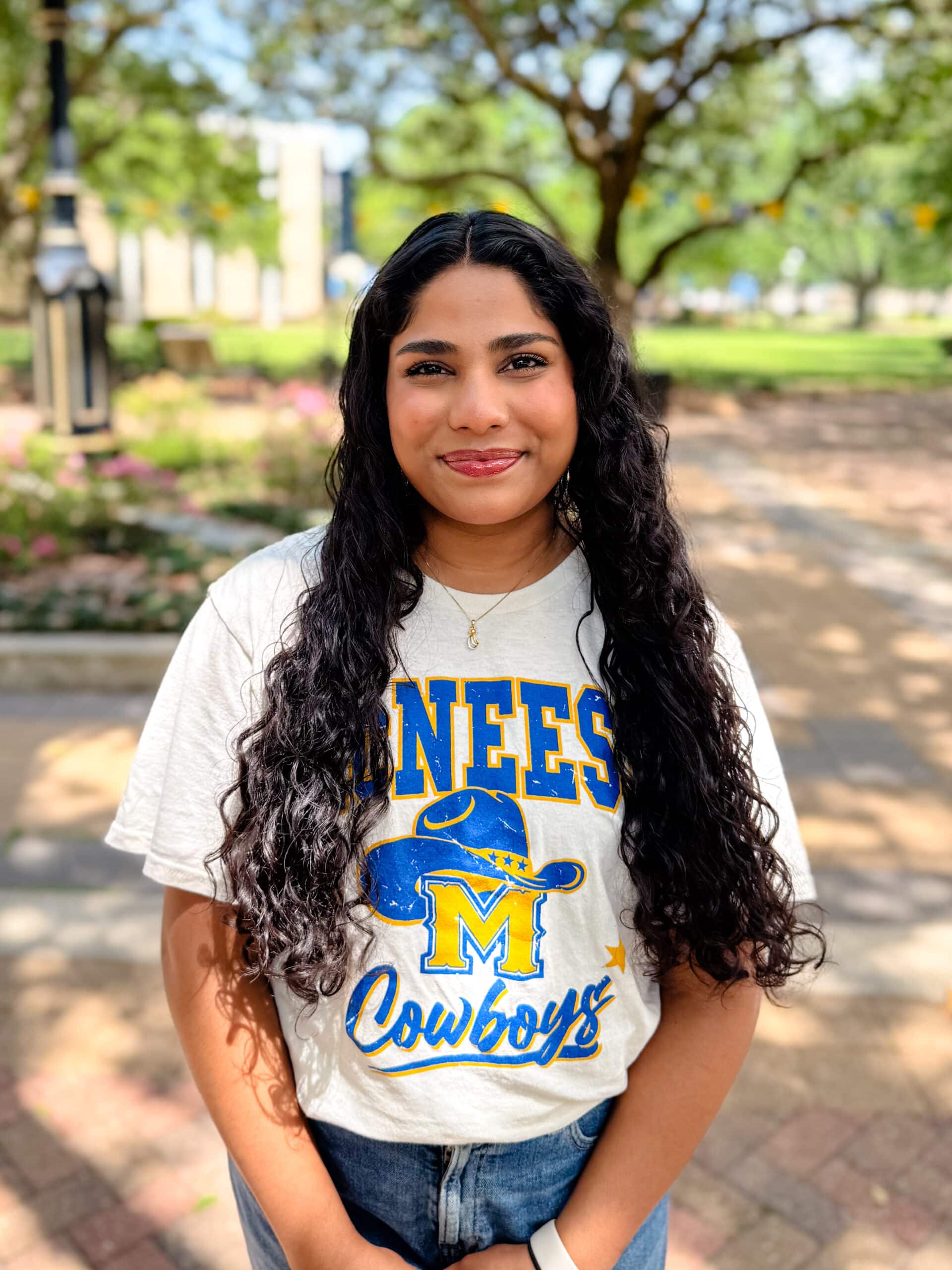 Susanna Chiruguru smiling outdoors in front of Clock Tower, wearing a white and blue T-shirt.