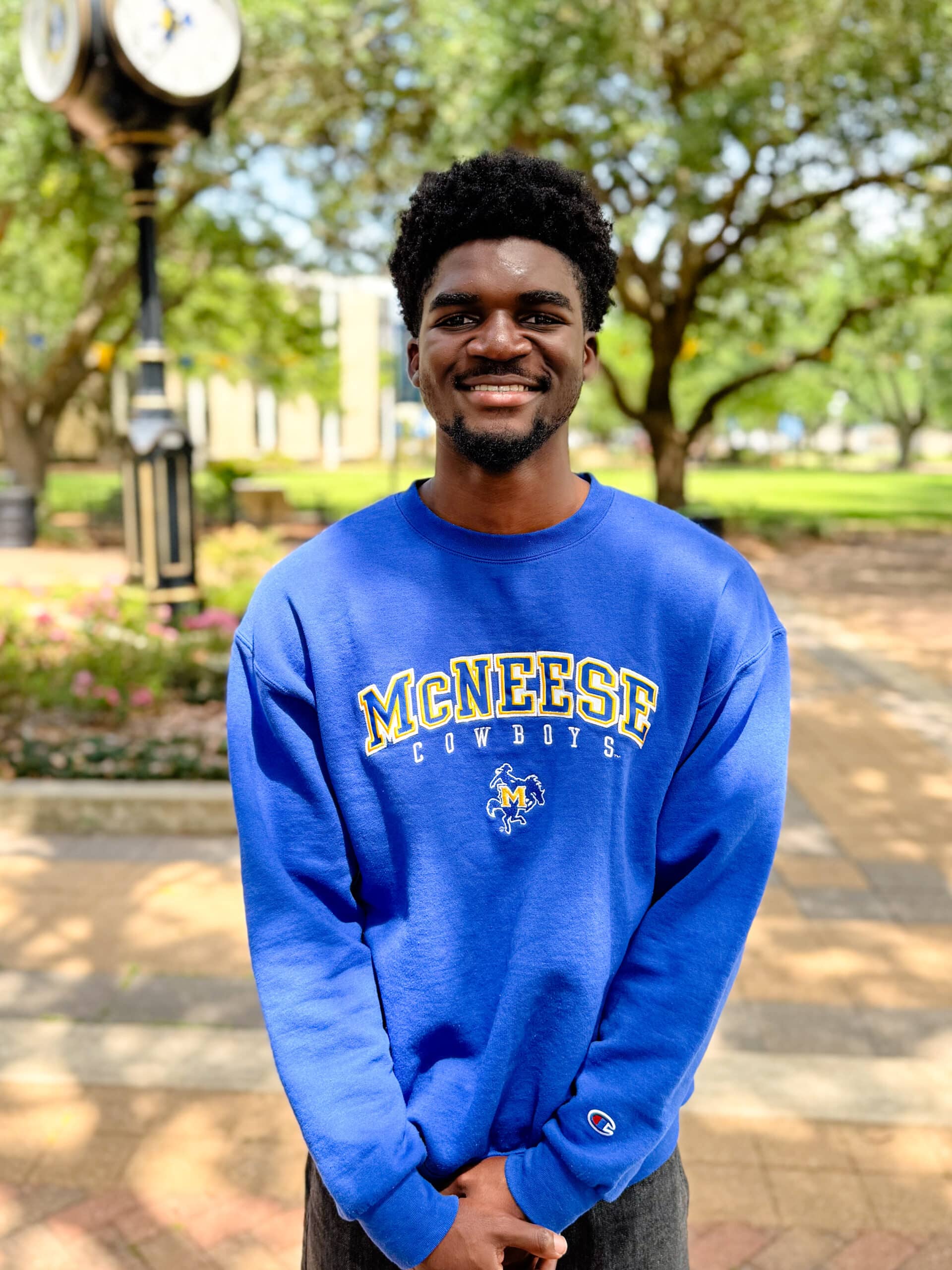 Victor Nwoye smiling outdoors in front of Clock Tower, wearing a long sleeve blue shirt.