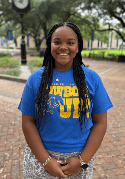 Victoria Clophus smiling outdoors in front of Clock Tower, wearing a blue and yellow T-shirt.