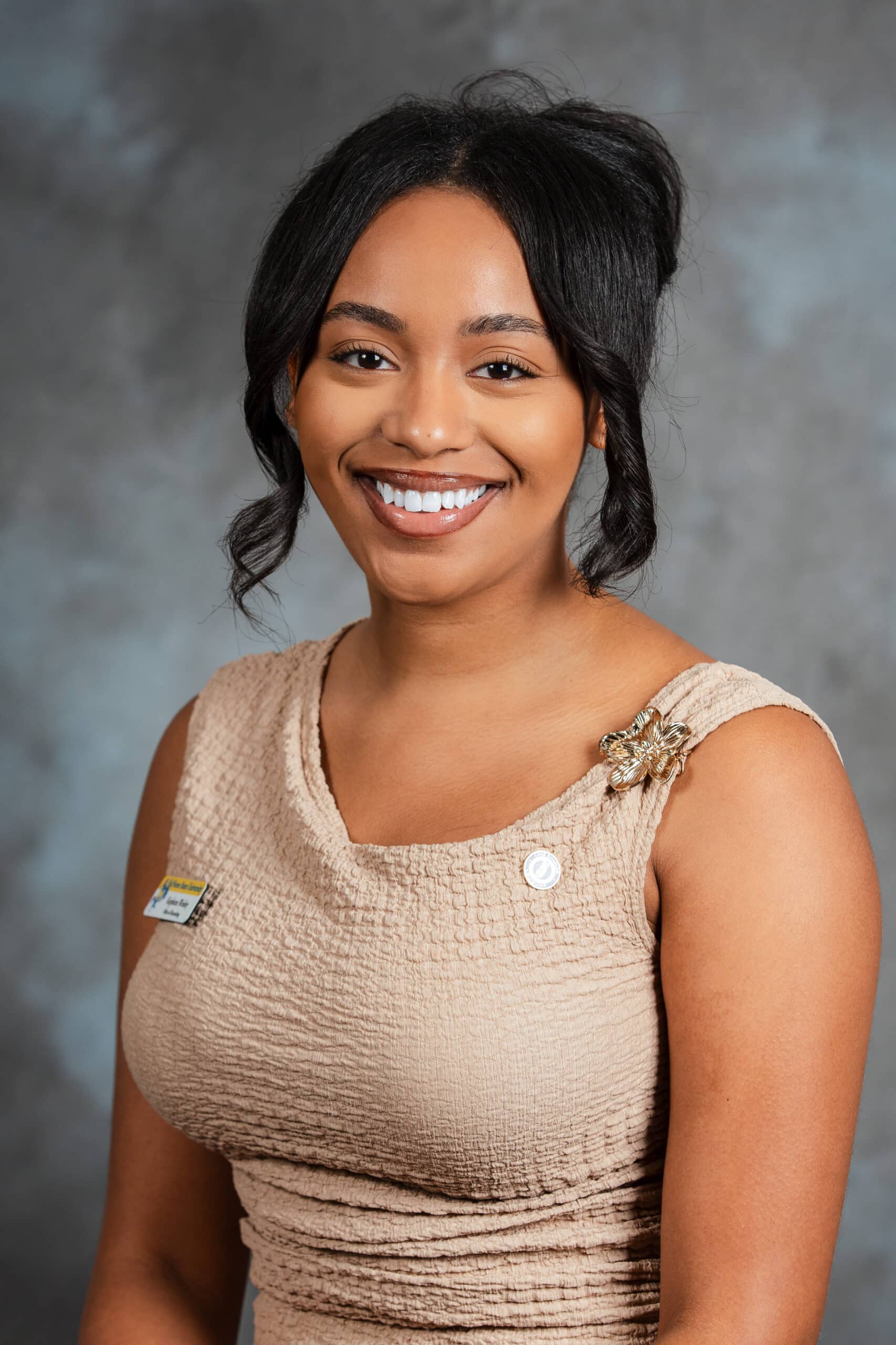 Woman smiling, wearing tan shirt against a gray studio background.